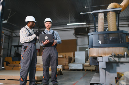 Two workers in a furniture factory collaborate on sofa production using a cnc machine, showcasing...