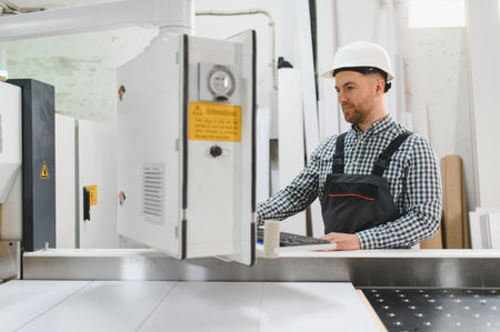 Carpenter wearing safety helmet operating a cnc machine in a furniture factory, focusing on...