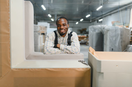 Portrait of a smiling African American worker in a furniture factory, leaning on a sofa during...