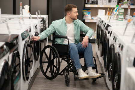 Man in wheelchair choosing washing machine in home appliance store, checking features before making purchaseの写真素材