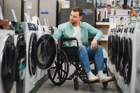 Man in wheelchair choosing washing machine in home appliance store, checking product features before making purchaseの写真素材