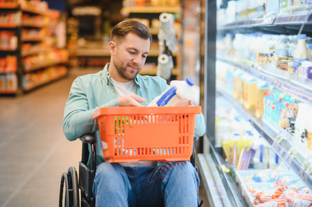 Man in wheelchair buying groceries, putting milk bottle in shopping basket in supermarket refrigerator sectionの写真素材