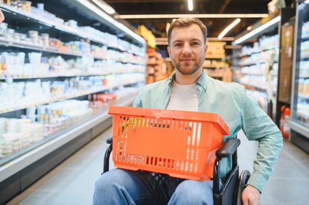 Smiling man sitting in wheelchair holding shopping basket while buying groceries in supermarketの写真素材