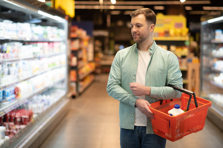 Man buying groceries in supermarket, walking through refrigerated section with shopping basketの写真素材