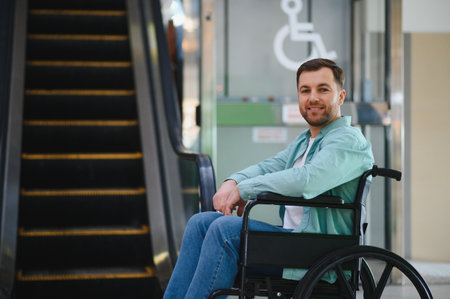 Portrait of a smiling man using a wheelchair in a shopping mall next to an escalator, promoting accessibility and inclusion for people with disabilitiesの写真素材
