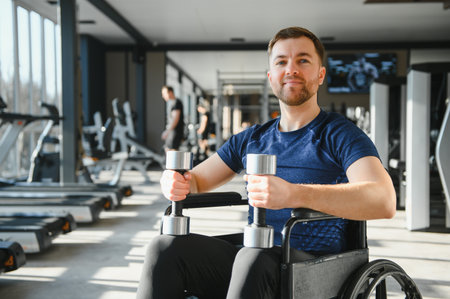 Man with disability exercising with dumbbells in a wheelchair at modern gym, undergoing rehabilitation treatment and demonstrating sports inclusionの写真素材