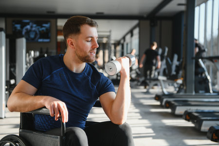 Determined male athlete in a wheelchair lifting a dumbbell, exercising his arm in a bright and...