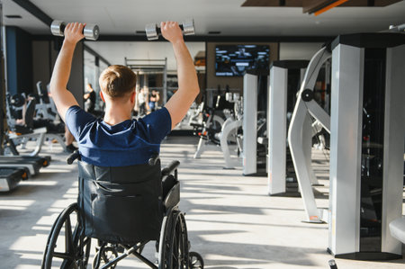 Man in wheelchair lifting weights during a rehabilitation workout in a modern gym, showing...