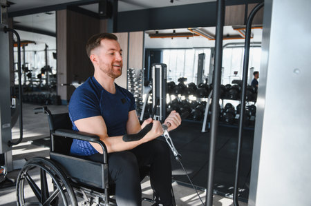 Smiling man using weights machine in wheelchair, working out biceps at gym, exercising for rehabilitation and physical therapyの写真素材