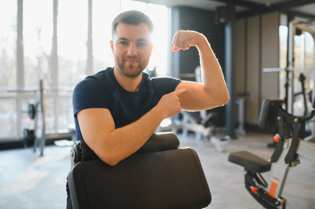 Strong man in wheelchair flexing biceps while seated in rehabilitation gym, embodying determination...