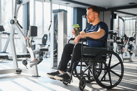 Caucasian man in wheelchair drinking from water bottle, resting after exercising in a modern bright...