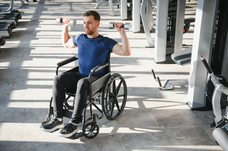 Man with disability exercising with dumbbells in a wheelchair, showing determination and strength during rehabilitation in a modern gymの写真素材