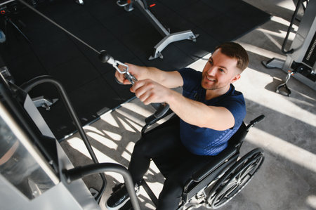 Man in a wheelchair engages in strength training at a gym, focusing on rehabilitation and fitness with specialized equipmentの写真素材