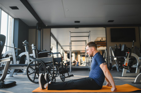 Person with disability exercising on a mat in a gym, with his wheelchair nearby, demonstrating perseverance and strengthの写真素材