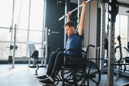 male athlete lifting weights while sitting in wheelchair, exercising and training in modern gym for rehabilitationの写真素材