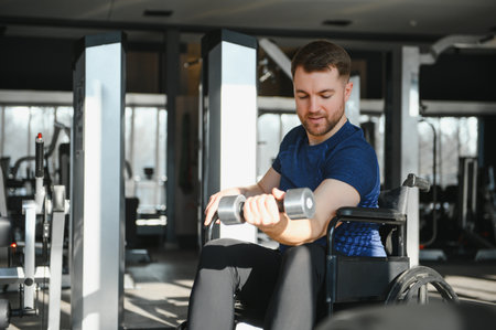 Man with disability exercising with dumbbells, sitting on a wheelchair in a gym, undergoing rehabilitation treatment and improving his physical conditionの写真素材