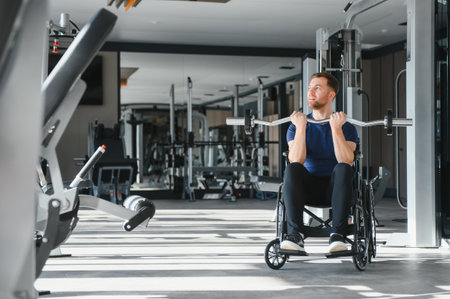 Person with disabilities using a wheelchair, lifting weights in a gym setting, highlighting sports rehabilitation and strength trainingの写真素材