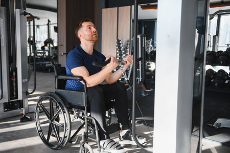 Determined male athlete in wheelchair exercising his arms using weights machine, demonstrating...