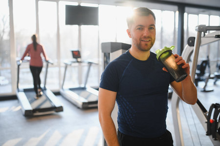 Smiling sportsman enjoying a sports nutrition supplement from a shaker while working out in a modern gym, embracing a healthy lifestyleの写真素材