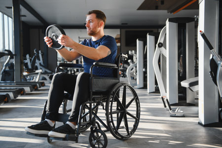 Caucasian man in wheelchair engaging in weightlifting during rehabilitation workout in a modern gym, showing determination and strengthの写真素材