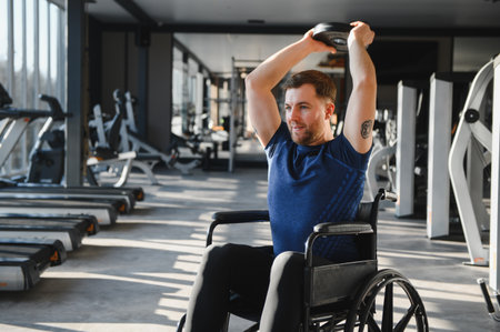 Man in a wheelchair lifting weights in a gym setting, focusing on fitness and rehabilitation. Emphasizes strength and determinationの写真素材