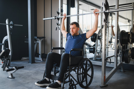 male athlete in wheelchair lifting weights during rehabilitation workout in modern gym,...