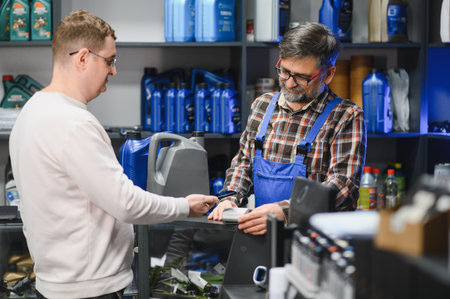 Mechanic holding pos terminal while customer making contactless payment with smartphone in auto...
