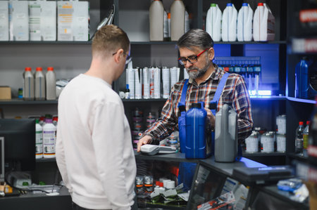 Mechanic holding and displaying various motor oils while assisting a customer with their purchase in...