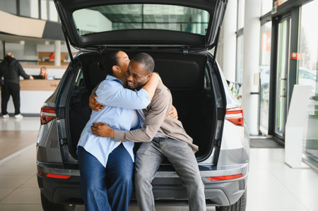 Excited couple hugging inside car trunk, celebrating their new vehicle purchase at dealership showroomの写真素材