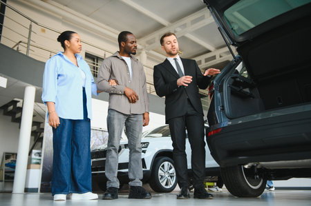 Car salesman showing the trunk of a new car to a couple in a dealership, offering a comprehensive...