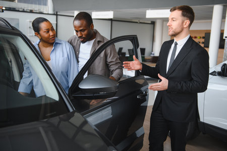 Car salesman presenting features of a new car to an African American couple, helping them make an...