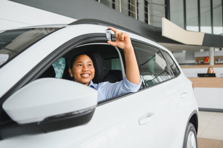 Excited customer sitting inside her new vehicle at a car dealership, proudly holding car keys and...
