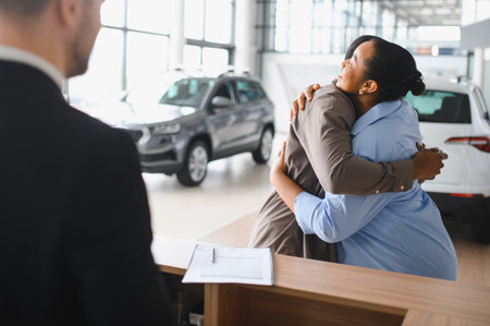Excited couple hugging at car dealership after buying their new car, embracing joy and achievementの写真素材