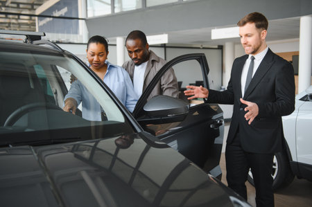 Car salesman engaging with a couple, highlighting features of a new car in a modern dealership...