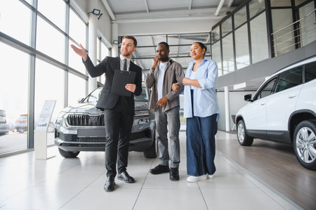 Car salesman presenting new vehicles to a couple in a car dealership, helping them choose the right...