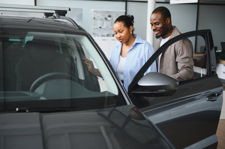 African american couple examining the interior of a new car in dealership showroom, considering purchase and discussing featuresの写真素材