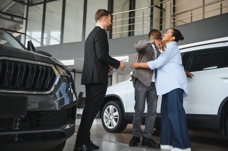 Car salesman handing over documents to a happy African American couple buying a new car in a...