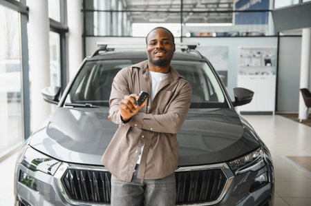Smiling customer proudly displaying car key in front of new vehicle at dealership, celebrating...