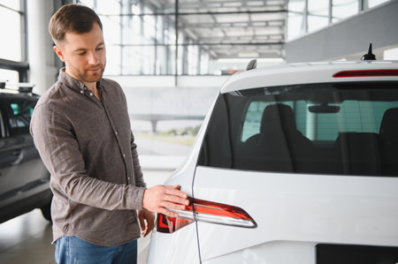 Man checking a white car's taillight in a car dealership showroom, considering his purchase optionsの写真素材