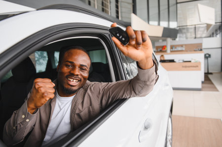 Happy african american customer showing car keys while sitting in his new vehicle at a car dealership, celebrating his purchaseの写真素材