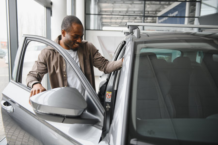 Happy customer smiling while examining a new car in a dealership showroom, touching the door and feeling proud of the purchaseの写真素材