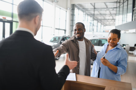 Happy african american couple shaking hands with a salesman after buying new car in a dealershipの写真素材