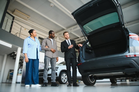 Car salesman guiding a couple through the trunk space of a new car in a vibrant dealership, discussing features and options togetherの写真素材
