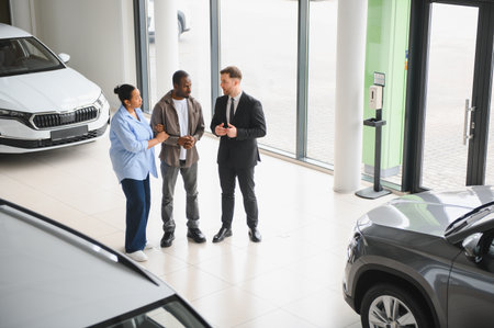 Car salesman presenting vehicles to african american couple in modern car dealership, offering...