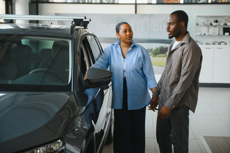 African american couple holding hands, discussing options while selecting a new car in a vibrant dealership showroom filled with vehiclesの写真素材