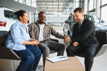 Smiling couple shaking hands with a salesman, celebrating the purchase of a new car in a bright and...