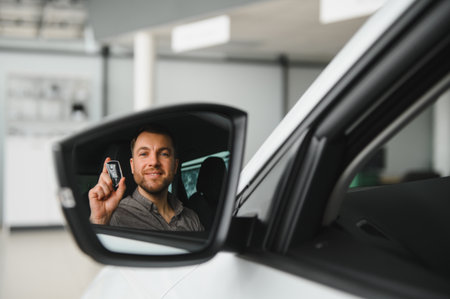 Customer sitting inside a modern car, proudly holding the key while enjoying a moment of reflection in the side mirror, radiating happinessの写真素材