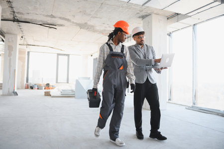 Architect showing information on a laptop to a builder walking inside a building under construction