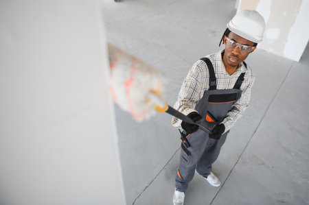African american construction worker painting walls with roller brush in a building under...