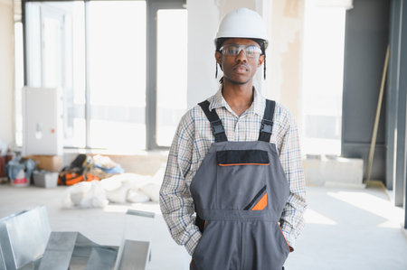 Young african american construction worker wearing work overalls, hardhat and protective glasses...